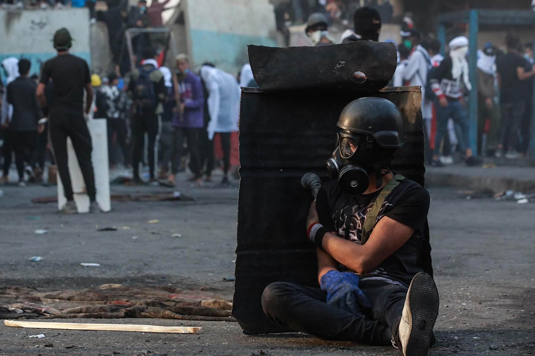 An Iraqi protester takes cover behind a shield during a violent anti-government protest on al-Rasheed Street in Baghdad, Iraq. 