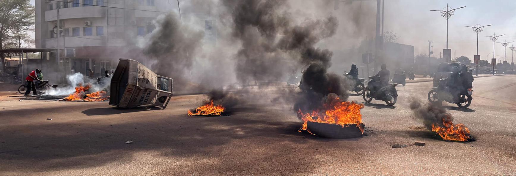 Commuters ride their motorcycles through burning barricades in the central avenues in Ouagadougou where group of young demonstrators supporting the role of the army protested against President Marc Christian Kabore on January 23, 2022.